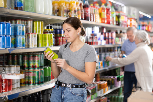 Portrait of thoughtful young girl choosing soft drinks while shopping in supermarket..