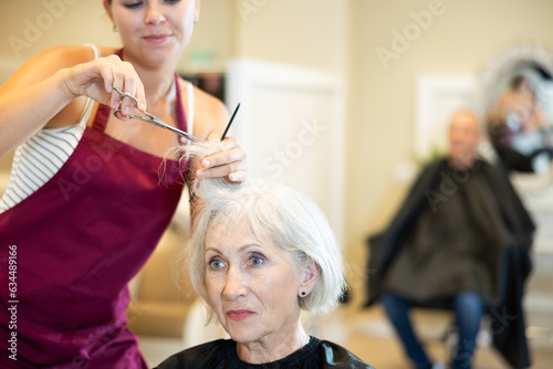 Young girl hairstylist working with female hair in hairdressing salon