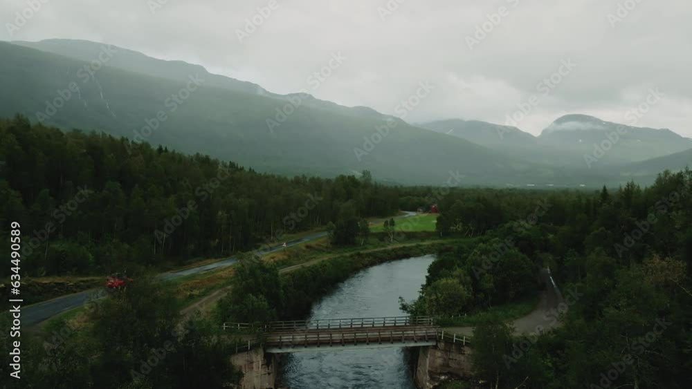 Epic moody panorama of beautiful wild nordic forest and river landscape. Red SUV driving down the wet roadway.
