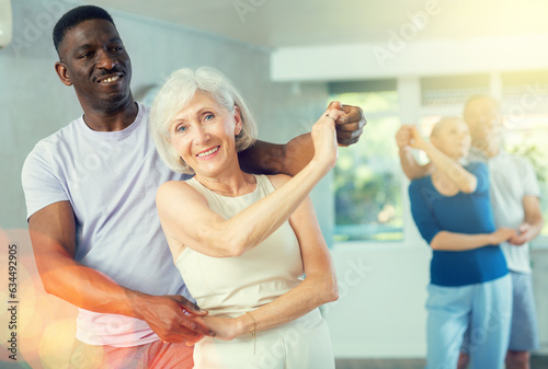 Fototapeta Naklejka Na Ścianę i Meble -  African man dances in couple with senior lady and learns Latin dance with other students. Physical activity, good bodily shape