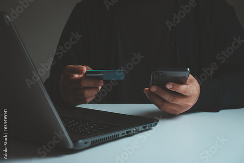 shopping online concept. Young adult male hands holding using mobile smartphone and credit card making online payment with laptop computer on table while holiday