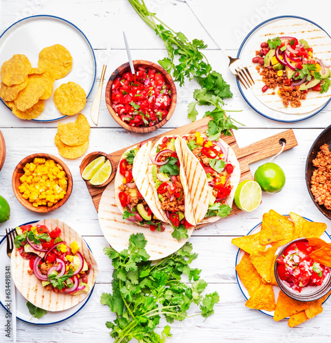 Taco party.  Served table with tortillas, nachos, sauces, appetizers and plates. Homemade mexican food cooking scene. White table background, top view