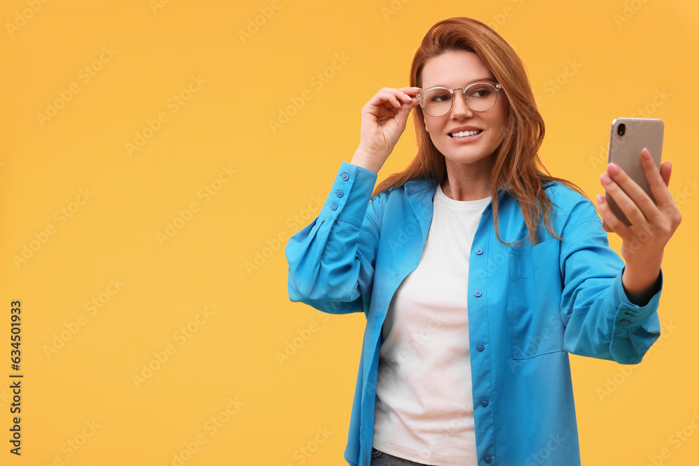 Beautiful woman in eyeglasses taking selfie on orange background. Space for text Beautiful woman in eyeglasses taking selfie on orange background. Space for text
