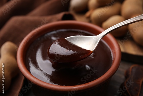 Taking tasty tamarind sauce with spoon from bowl on table, closeup