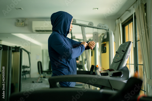 Athletic Asian Muslim Sports Woman Wearing Hijab and Sportswear Running on Treadmill. Energetic Fit Female Athlete Training in Gym Alone. Urban Business District Window View. concept of muslim sport.