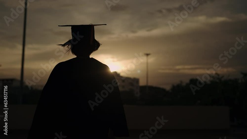 Study, education, university, college, graduate concept. Portrait of a cheerful Asian female in academic gown and graduation hat standing outside college. photo
