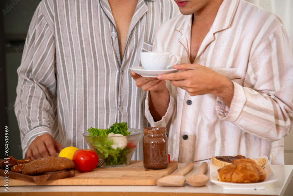 Happy gay couple enjoy breakfast in kitchen drinking coffee. Two best friends LGBTQ relation partner home cooking. Happiness romance homosexual marriage lifestyle. Two men together love friendship.