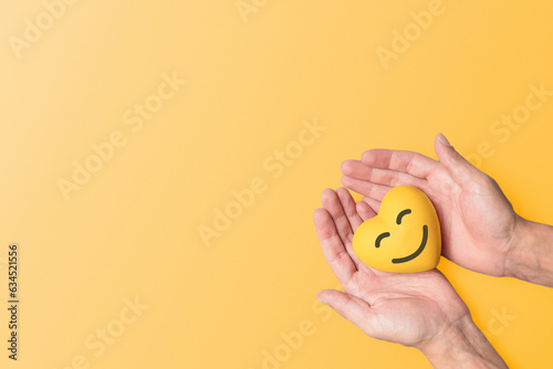  hands  holding a yellow resin heart against a matching yellow background, symbolizing mental health awareness and the significance of September Yellow.  Mental wellbeing and suicide prevention.  photo