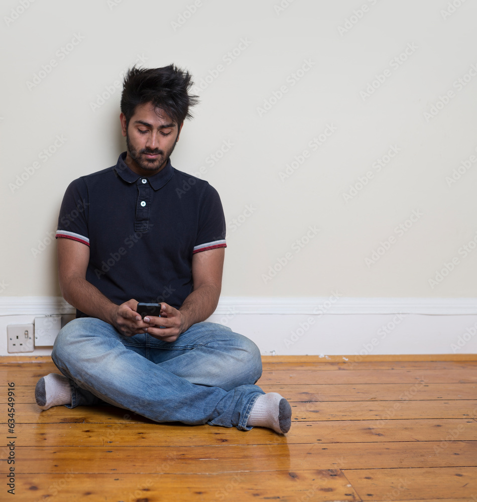 Indian Man sitting on floor using his phone.