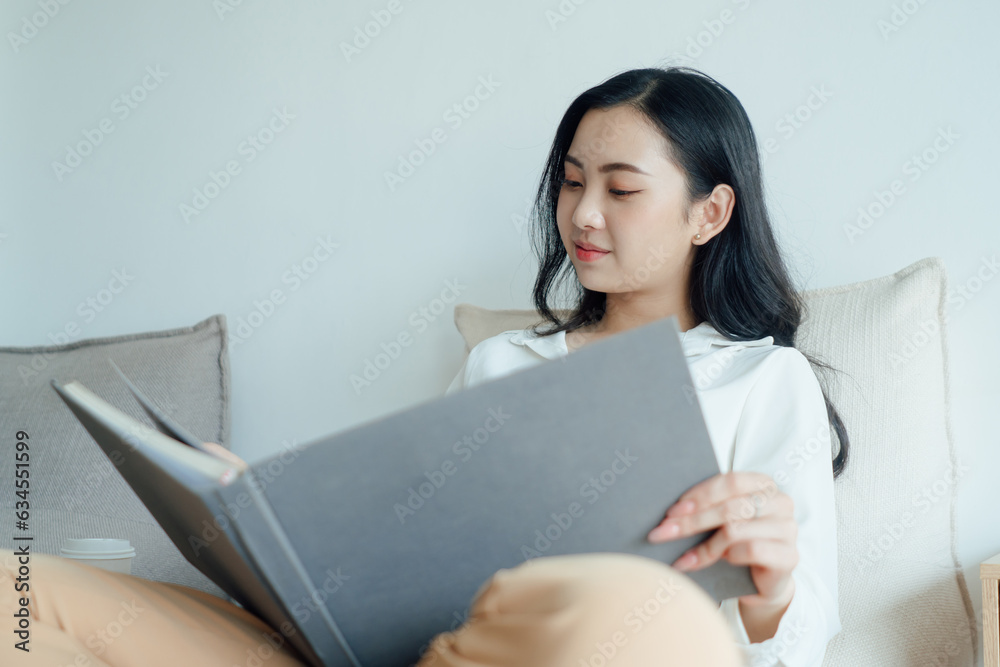 Relaxing woman with long wavy hair with books in modern living room on sunny day.Beautiful young lady reading exciting story, enjoying lazy morning, having relaxing weekend Relaxing woman with long wavy hair with books in modern living room on sunny day.Beautiful young lady reading exciting story, enjoying lazy morning, having relaxing weekend