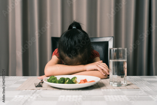 Little cute kid girl refusing to eat healthy vegetables. Children do not like to eat vegetables. photo