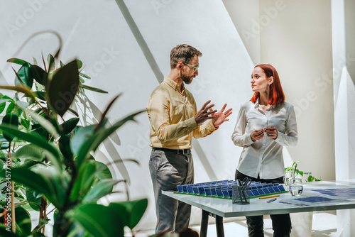 Businessman explaining and having discussion with colleague over solar panel model in office