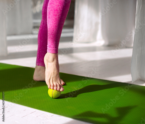 Massage for feet  with tennis ball. Woman practicing foot self-massage with a tennis ball. Physiotherapy, reflexology. Tension relieving in the plantar fascia. Improving foot joint mobility.