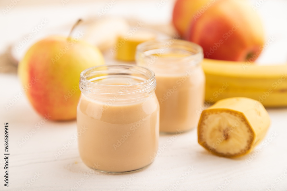 Baby puree with fruits mix, apple, banana infant formula in glass jar on white, side view, selective focus Baby puree with fruits mix, apple, banana infant formula in glass jar on white, side view, selective focus