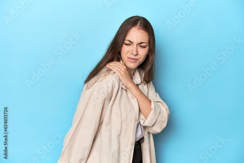 Stylish young woman in an overshirt on a blue background having a shoulder pain.