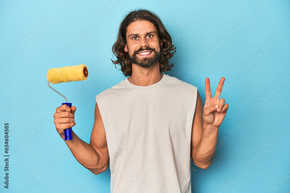 Bearded man painting with a yellow roller showing number two with fingers. Bearded man painting with a yellow roller showing number two with fingers.