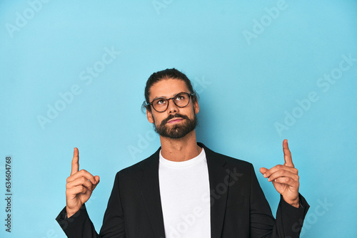 Businessman in suit with eyeglasses and beard pointing upside with opened mouth.