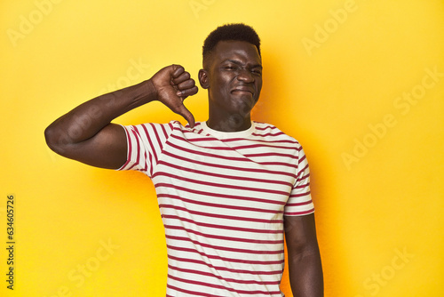 Stylish young African man on vibrant yellow studio background, showing thumb down, disappointment concept.