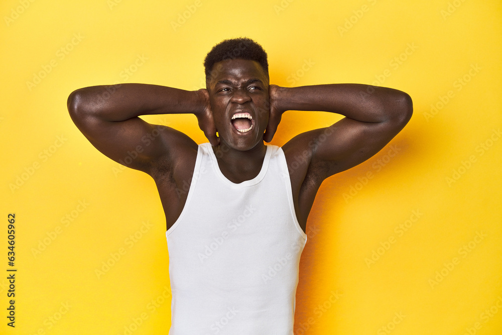 Stylish young African man on vibrant yellow studio background, covering ears with hands trying not to hear too loud sound. Stylish young African man on vibrant yellow studio background, covering ears with hands trying not to hear too loud sound.