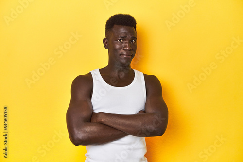 Stylish young African man on vibrant yellow studio background, unhappy looking in camera with sarcastic expression.