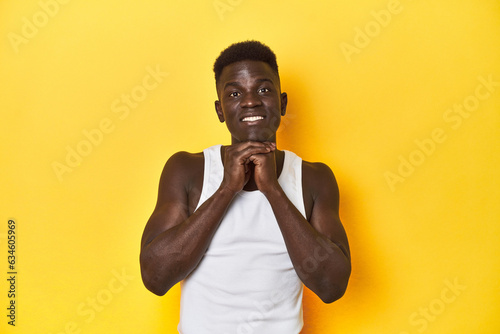 Stylish young African man on vibrant yellow studio background  praying for luck  amazed and opening mouth looking to front.