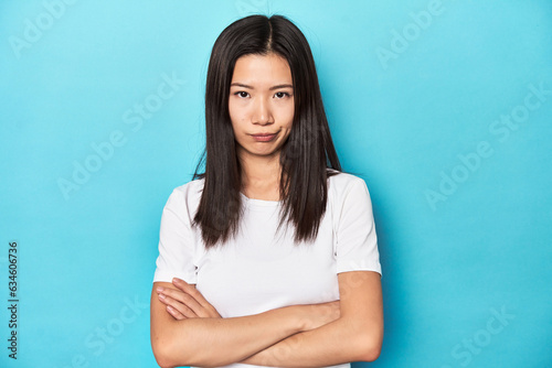 Young Asian woman in white t-shirt, studio shot, unhappy looking in camera with sarcastic expression.