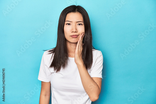 Young Asian woman in white t-shirt, studio shot, having a strong teeth pain, molar ache. © Asier