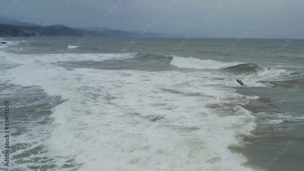 Waves crashing across itzurun beach in slow motion, aerial reverse dolly