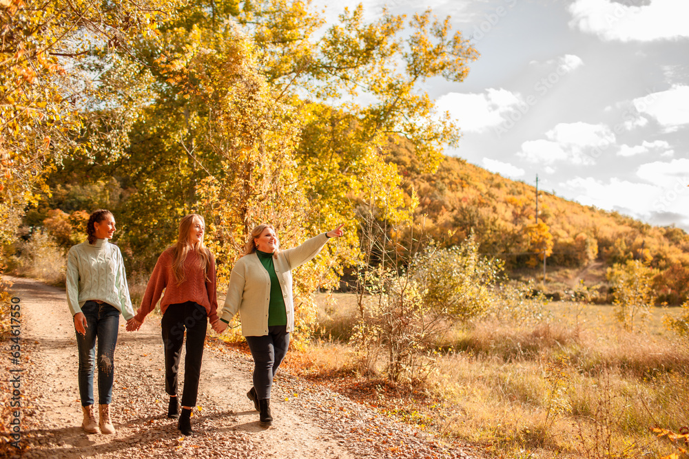 Obraz premium Multiracial female people with different bodies and hairs walking in the fall parks together. Friends wearing warm fashion clothes, knitted sweaters.