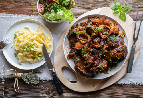 Braised beef shanks with buttered pasta. Delicious sunday or holiday dinner or lunch on wooden table from above