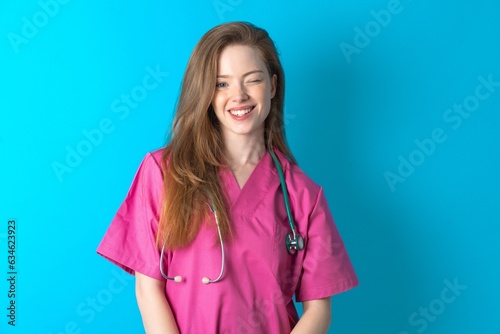 Coquettish Young caucasian doctor woman wearing pink medical uniform smiling happily, blinking at camera in a playful manner, flirting with you.