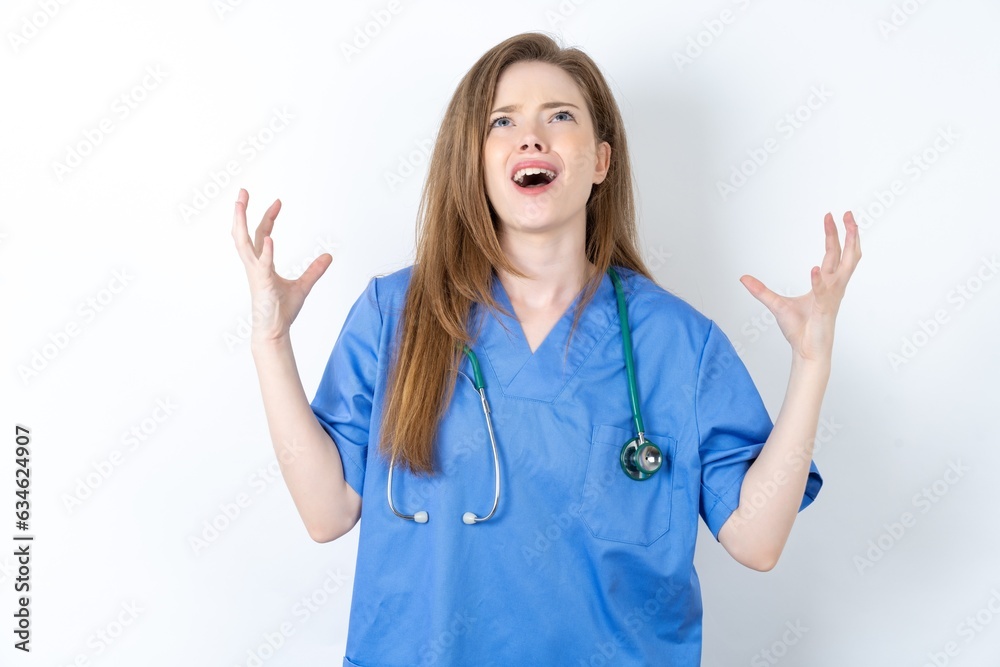 Young caucasian doctor woman wearing medical uniform crazy and mad shouting and yelling with aggressive expression and arms raised. Frustration concept.