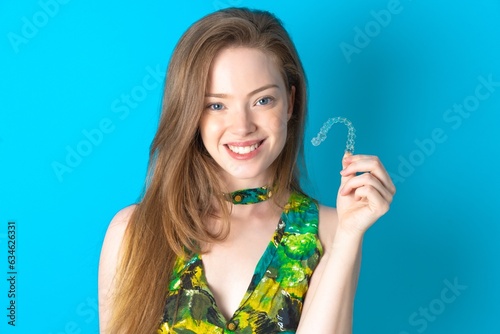 Young caucasian beautiful girl holding an invisible braces aligner, recommending this new treatment. Dental healthcare concept.