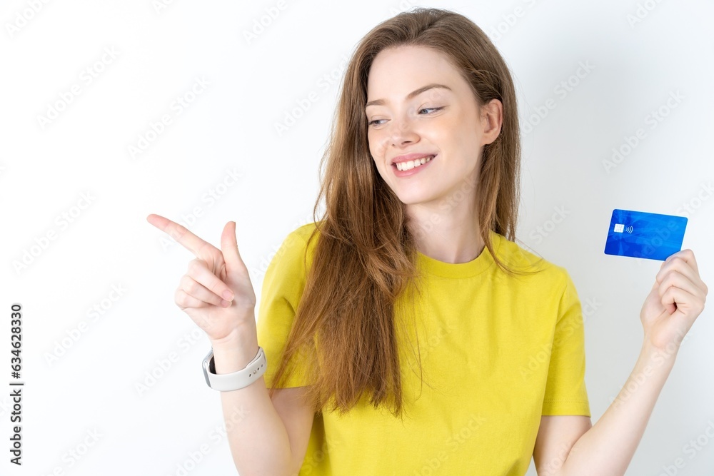Curious smiling Young beautiful girl wearing yellow T-shirt showing plastic bank showing finger copyspace Curious smiling Young beautiful girl wearing yellow T-shirt showing plastic bank showing finger copyspace
