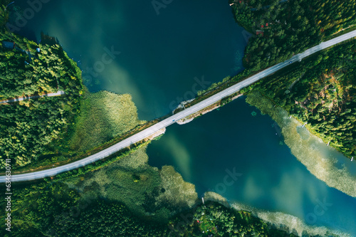 Fototapeta Naklejka Na Ścianę i Meble -  Aerial view of bridge asphalt road with cars and blue water lake and green woods in Finland.