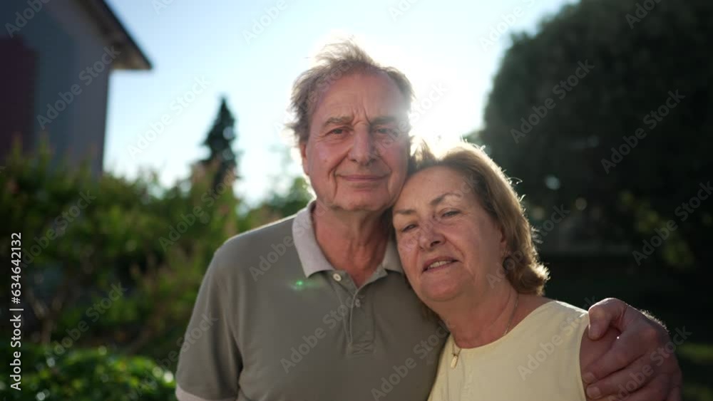Portrait of a Senior Couple standing outdoors with sun flare. Happy older husband with arm around wife posing to camera. Love and happiness concept Portrait of a Senior Couple standing outdoors with sun flare. Happy older husband with arm around wife posing to camera. Love and happiness concept