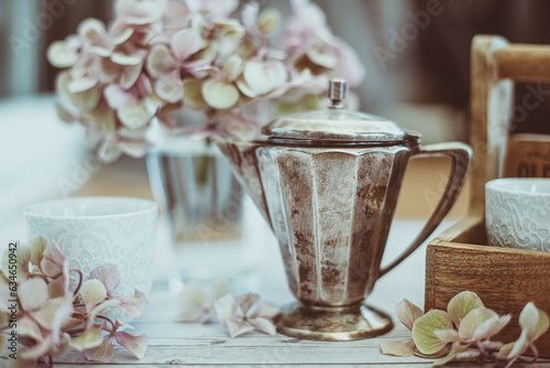 Vintage silver pot and teacups on a table with pink hydrangeas photo
