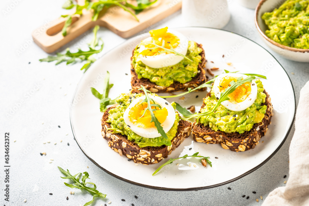 Open sandwich. Whole grain bread with avocado and boiled eggs. Top view on white kitchen table. Open sandwich. Whole grain bread with avocado and boiled eggs. Top view on white kitchen table.