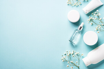 Natural cosmetic products at blue background. Cream, serum, tonic with green leaves and flowers. Flat lay image with copy space.