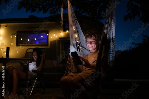 Delighted boy using smartphone in hammock outside trailer