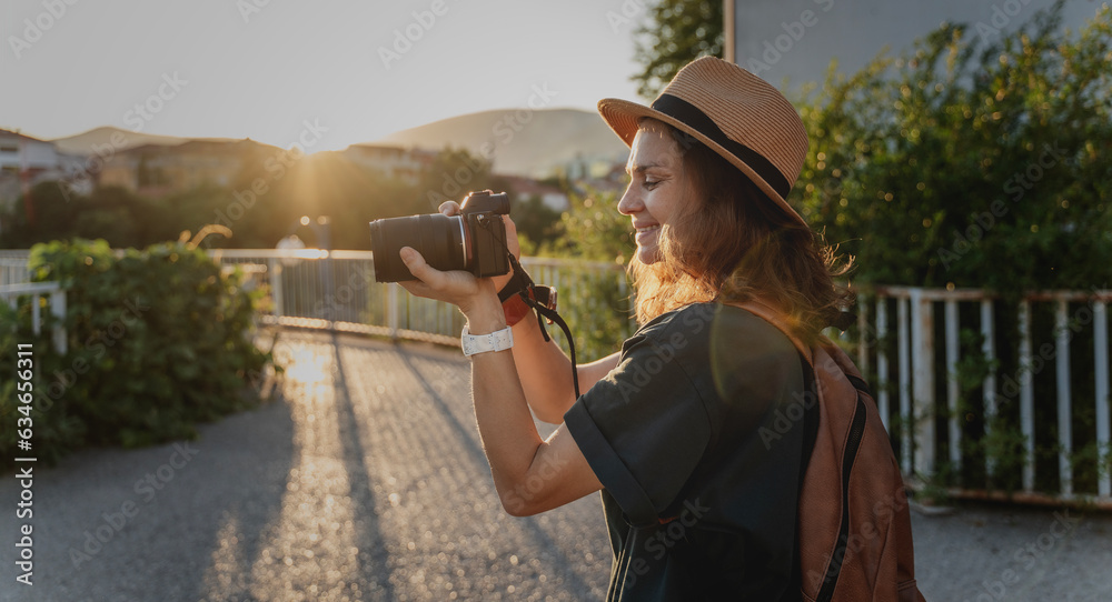 Young caucasian woman traveler in a hat with a photo camera in her hands in a summer city at sunset