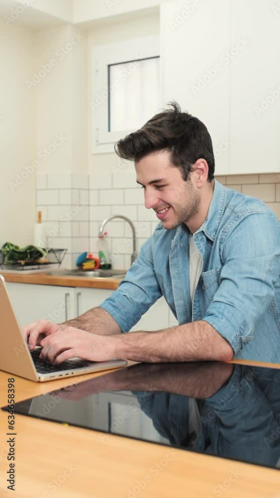 Handsome young man working with a laptop and smiling at the kitchen with a cup of tea - Cheerful, success and business concept
