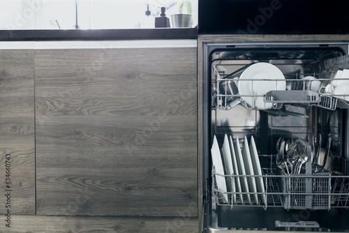 Closeup of opened automatic stainless built-in dishwasher machine inside modern home kitchen with clean utensil. Opening and closing washing machine. Lifestyle view of interior with kitchen appliances