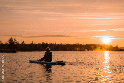 Stand up paddle boarding or standup paddleboarding on quiet lake at sunrise with beautiful colors during warm summer. Active women, close-up of water surface.