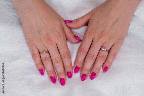 Close-up of well-groomed female pink nails. Beautiful clear fingers of a young girl with nice manicure and Glitter Nail Polish. Girl hands on a white background. Girl is wearing two diamond rings.