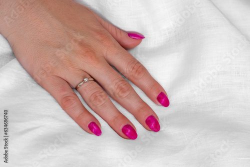 Close-up of well-groomed female pink nails. Beautiful clear fingers of a young girl with nice manicure and Glitter Nail Polish. Girl hands on a white background. Girl is wearing two diamond rings.