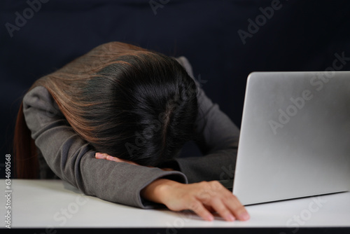 Mid adult businesswoman hands lying face down on table after bad news business failure or get fired and feeling discouraged, distraught and hopeless on blue background with computer and copy space.