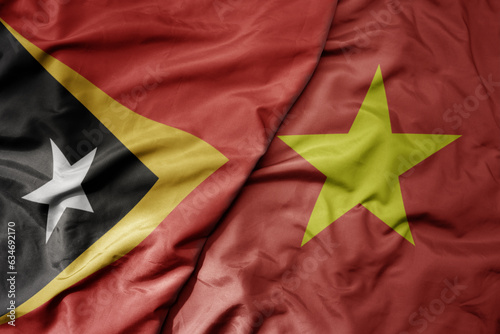 big waving realistic national colorful flag of east timor and national flag of vietnam .