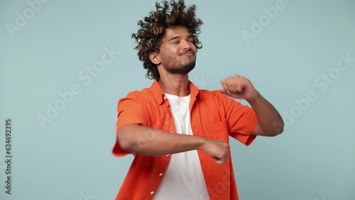 Young vivid happy bright Indian man wears red shirt casual clothes dance waving rising have fun enjoy relax celebrate play fluttering hair isolated on pastel plain light blue cyan background studio