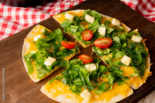 Arugula handmade pizza served in wooden cutting board above a wooden table with a red picnic cloth